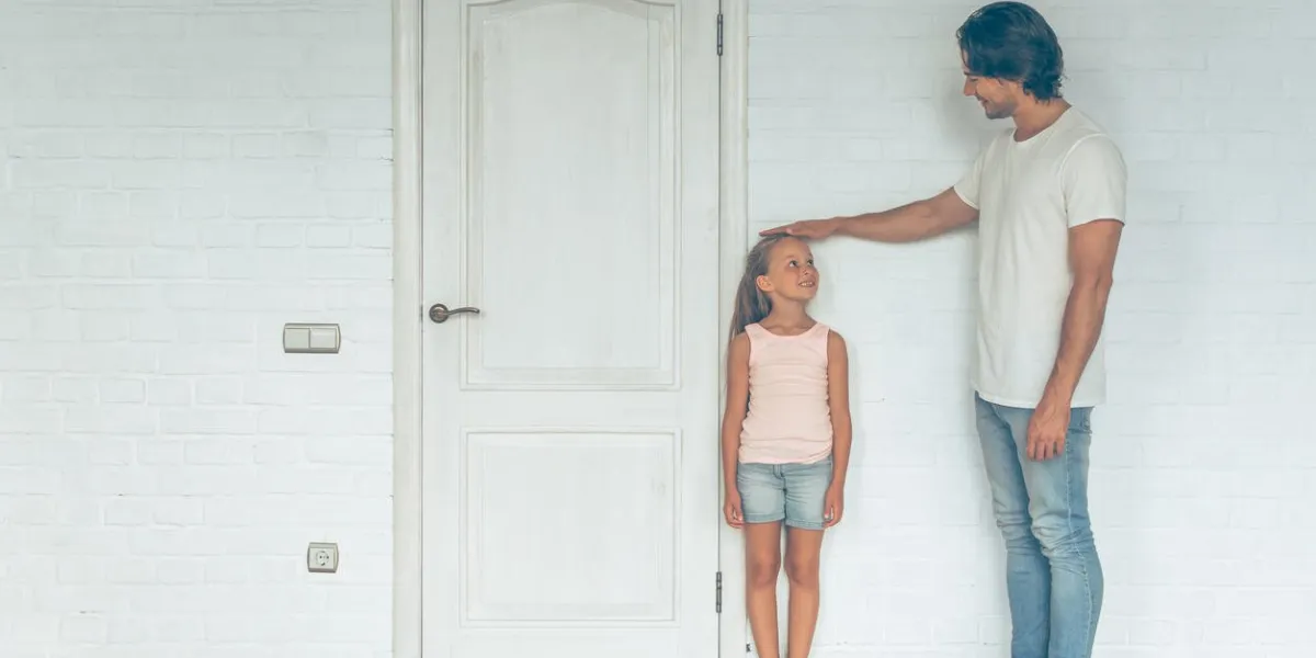 full length portrait of handsome father measuring height of his cute little daughter near the door at home both are looking at each other and smiling