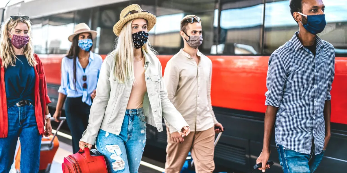 multiracial friends group walking at railway station platform - new normal travel concept with young travelers on social distancing and face covered by protective mask - focus on blonde girl with hat