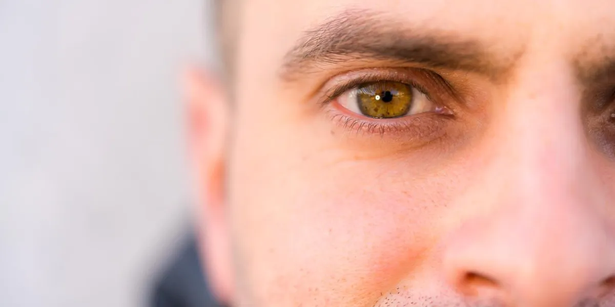 gros plan de l'oeil noisette de jeune homme regardant l'arrière-plan flou de la caméra