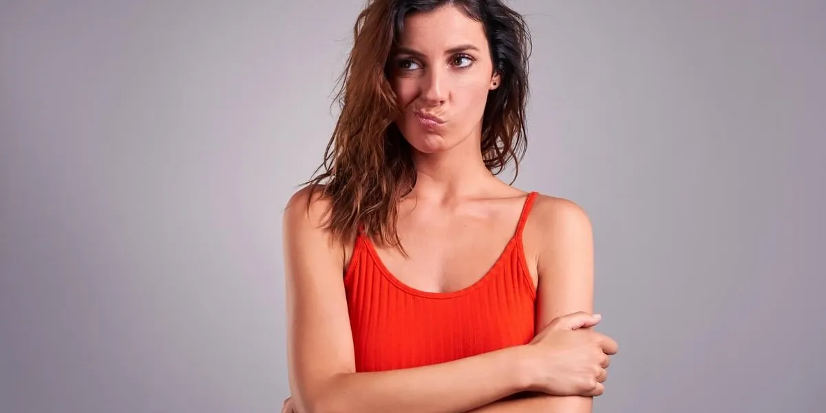 a beautiful young woman looking suspiciously and squeezing her mouth in a red top