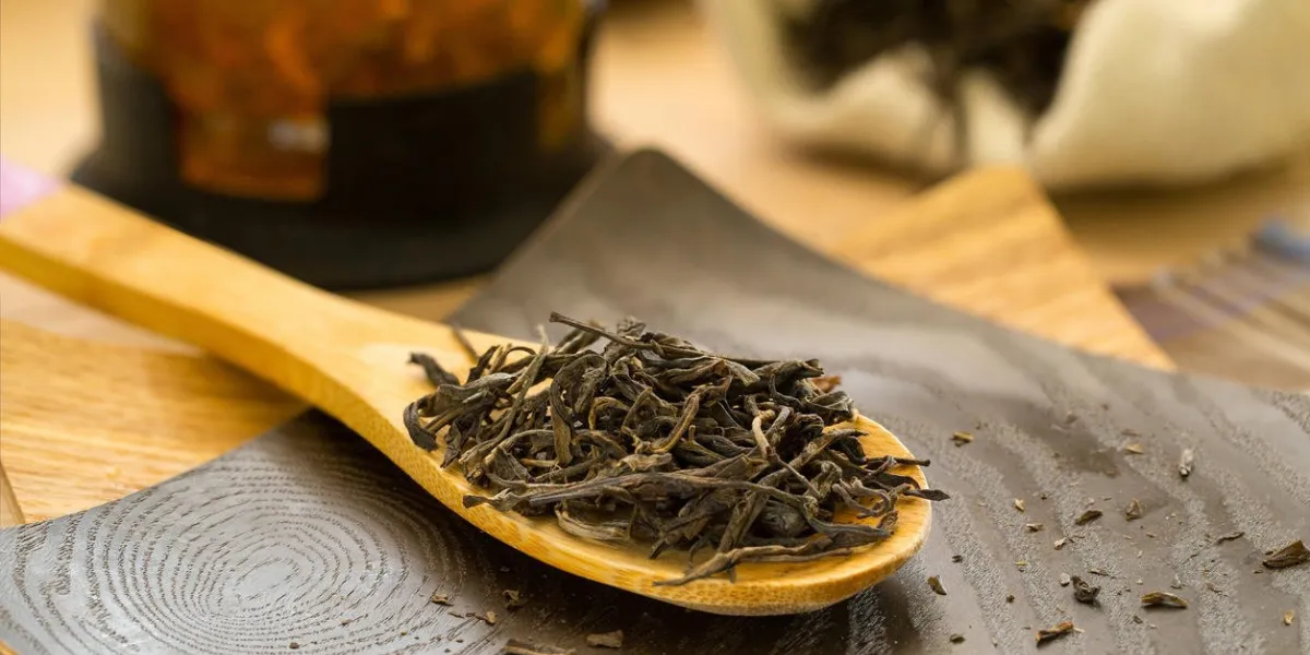 puerh de thé sec sur une cuillère en bois, théière et un sac de toile de jute en arrière-plan