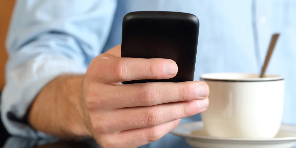 gros plan d'un homme à la main en utilisant un téléphone intelligent au petit déjeuner avec une tasse de café en arrière-plan