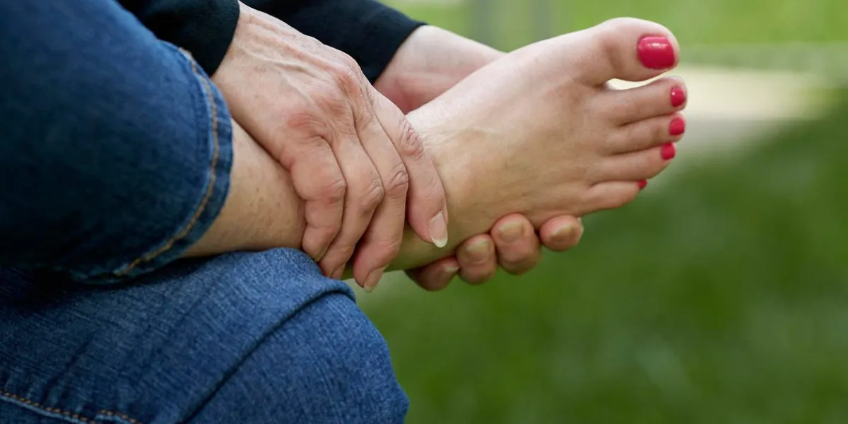 a woman's hand rubbing the sole of her foot while sitting in a chair outdoors with shallow depth of field