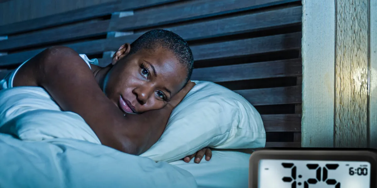 lifestyle portrait of young sad and depressed black afro american woman awake on bed sleepless suffering insomnia sleeping disorder and anxiety problem with alarm clock late night hour