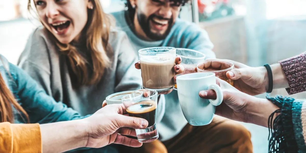 happy friends having breakfast together at cafe bar - group of young people drinking coffee and fresh juice sitting at brunch restaurant - food and drink concept