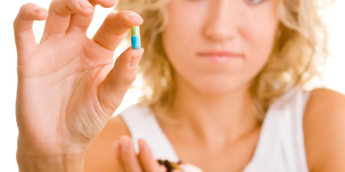 femme blonde tient une capsule colorée dans sa main