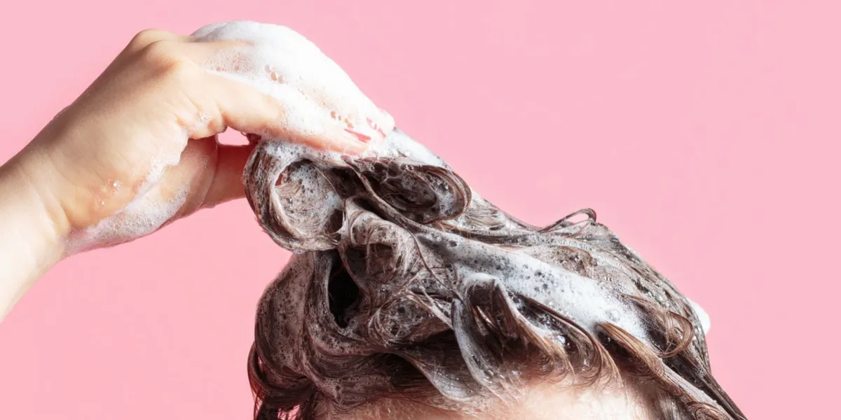 a girl washes her hair with shampoo on a pink background, front view