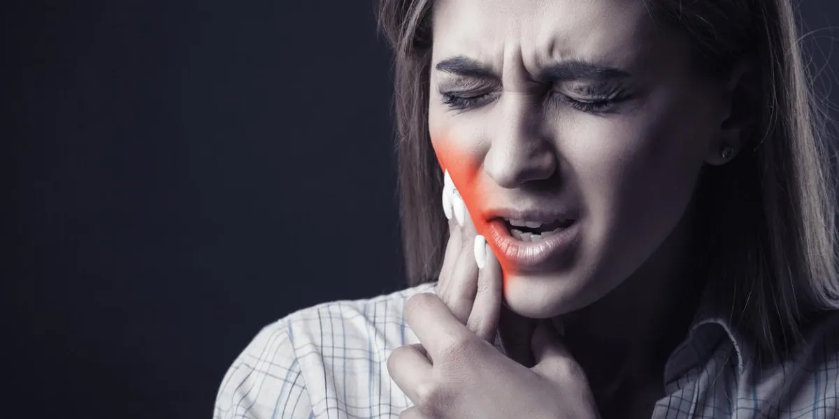 young woman is suffering from a toothache against a dark background