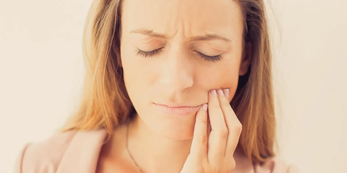 close-up of sad face of young caucasian businesswoman having toothache, touching her cheek