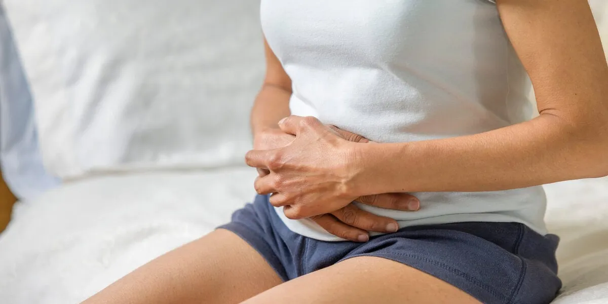 woman holding stomach with cramp or pain female mid adult asian indian, uk