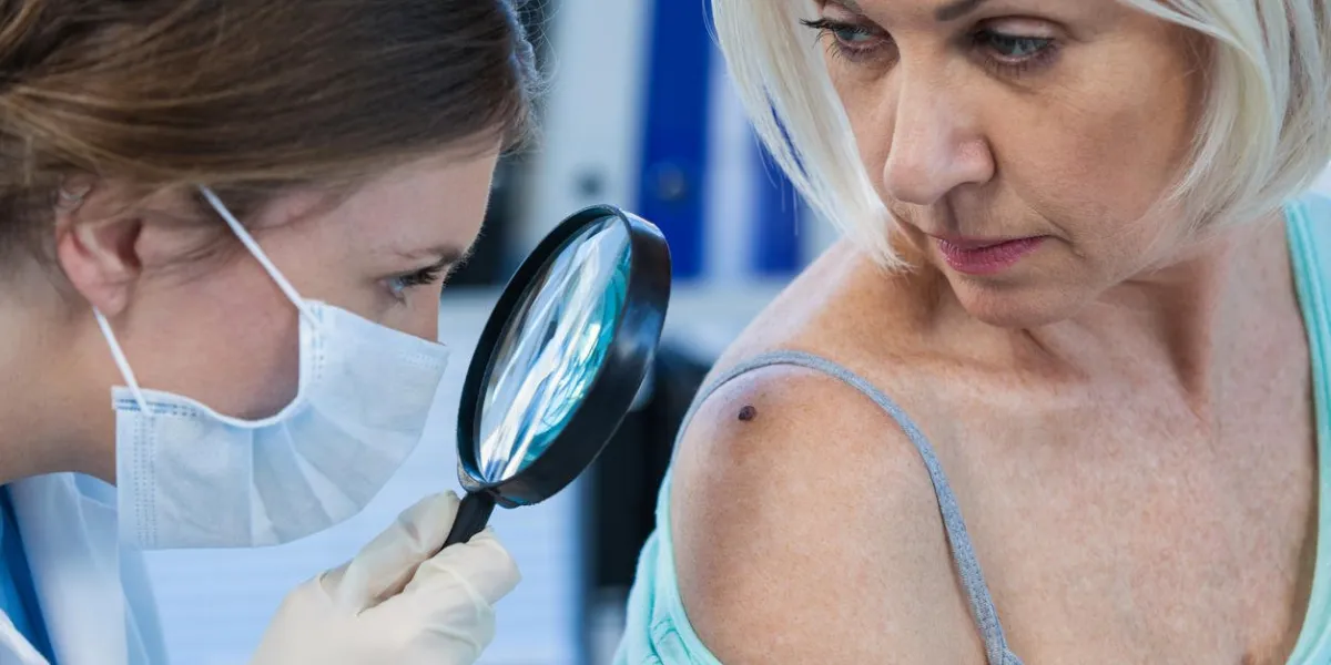 dermatologist examining mole of female patient with magnifying glass in clinic