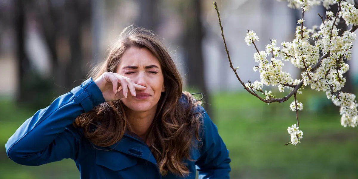 pretty young woman sneezing and having alergy symptoms from blooming tree pollen in early spring