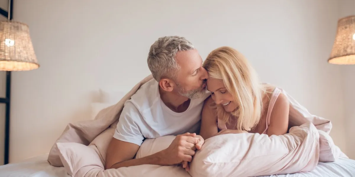 romance grey-haired man and a blonde woman lying on the bed and looking romantic
