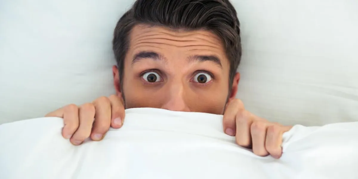 homme se cachant dans son lit sous la couverture à la maison