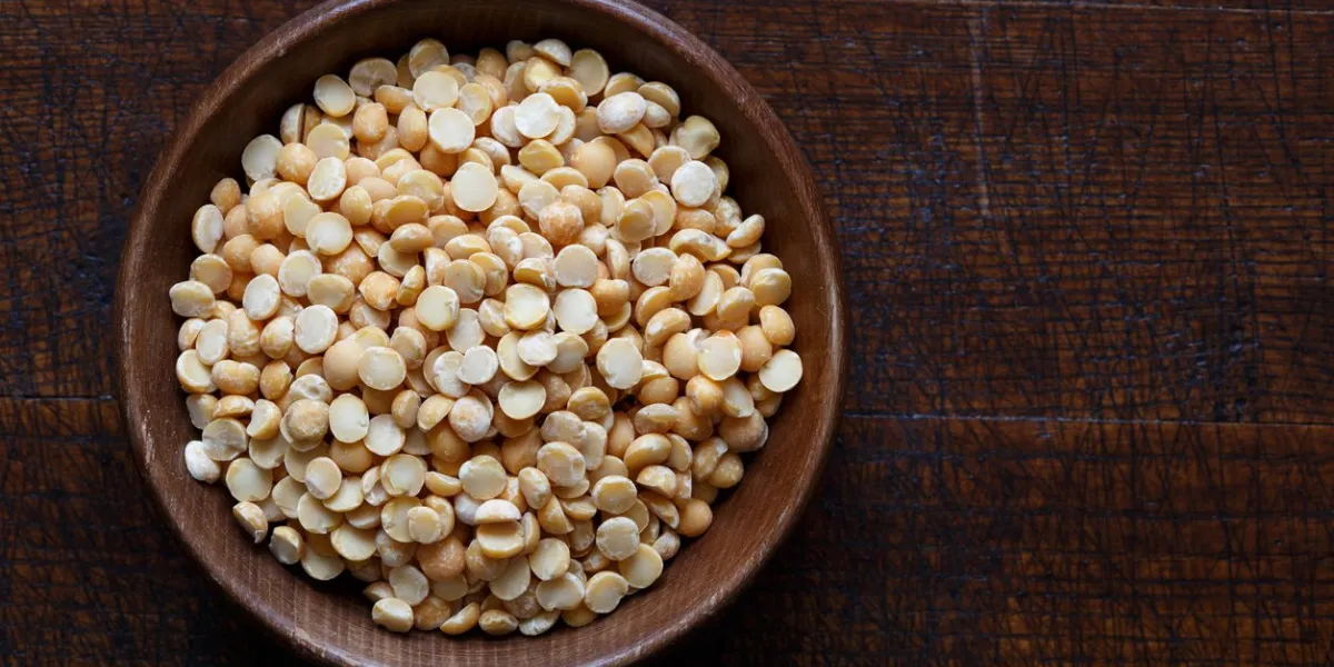 dry yellow split peas in brown wooden bowl isolated on dark wood from above