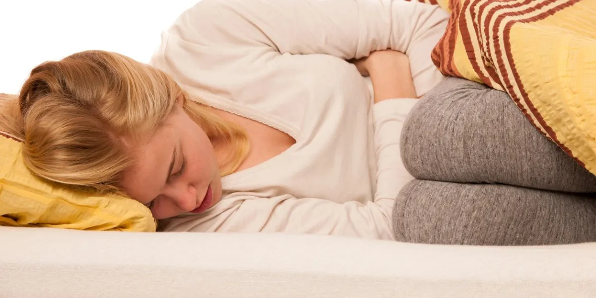 woman lying in bed holding belly because of the pain in stomach