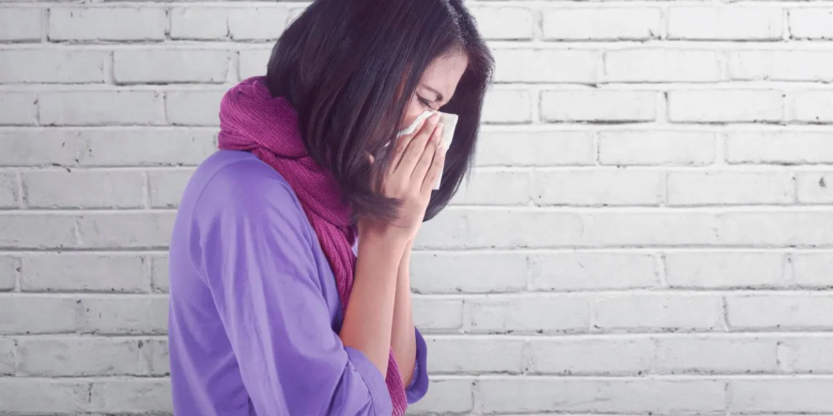 sick asian woman with flu and fever holding tissue in nose against wall background
