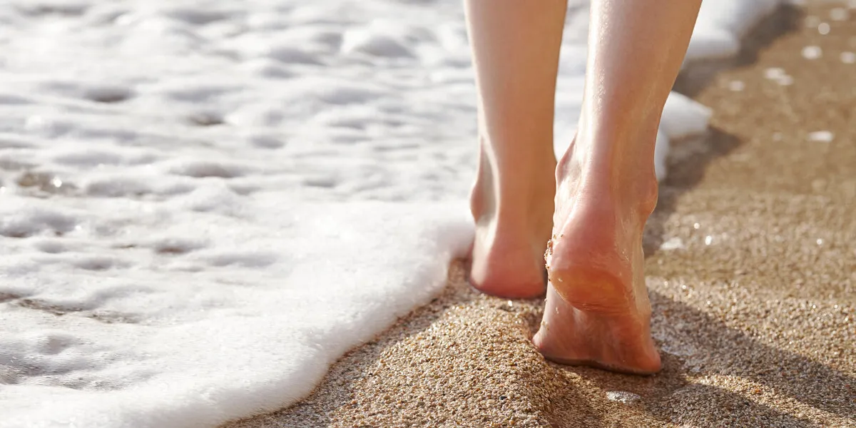 woman walking on a beautiful sandy beach during sunset, feet close up view