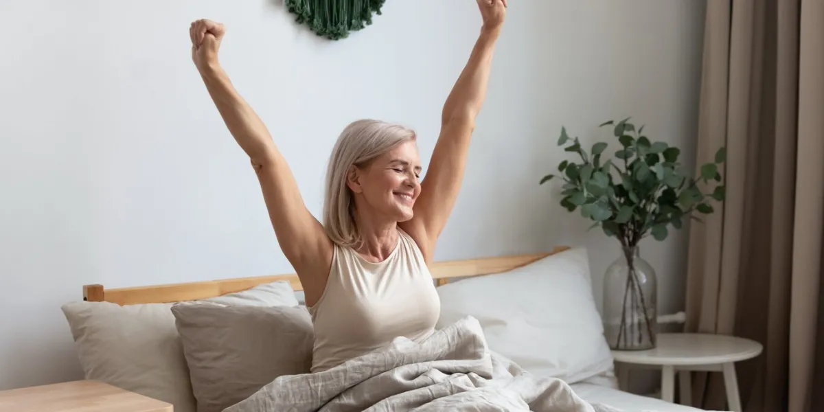 active happy mature female wake up from good healthy sleep stretching sitting in bed at home, smiling positive senior woman awaken in comfortable bedroom feel optimistic welcome new day