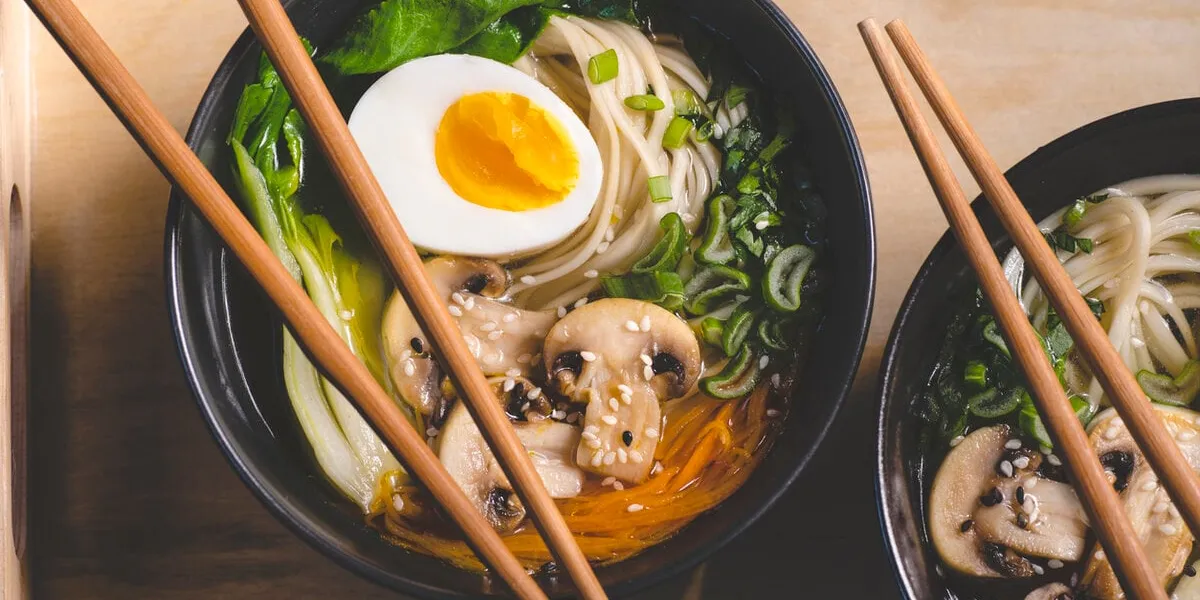traditional japanese ramen soup with mushrooms, bok choy, greens in two black bowls on the orange background, top view, close up japanese cuisine concept