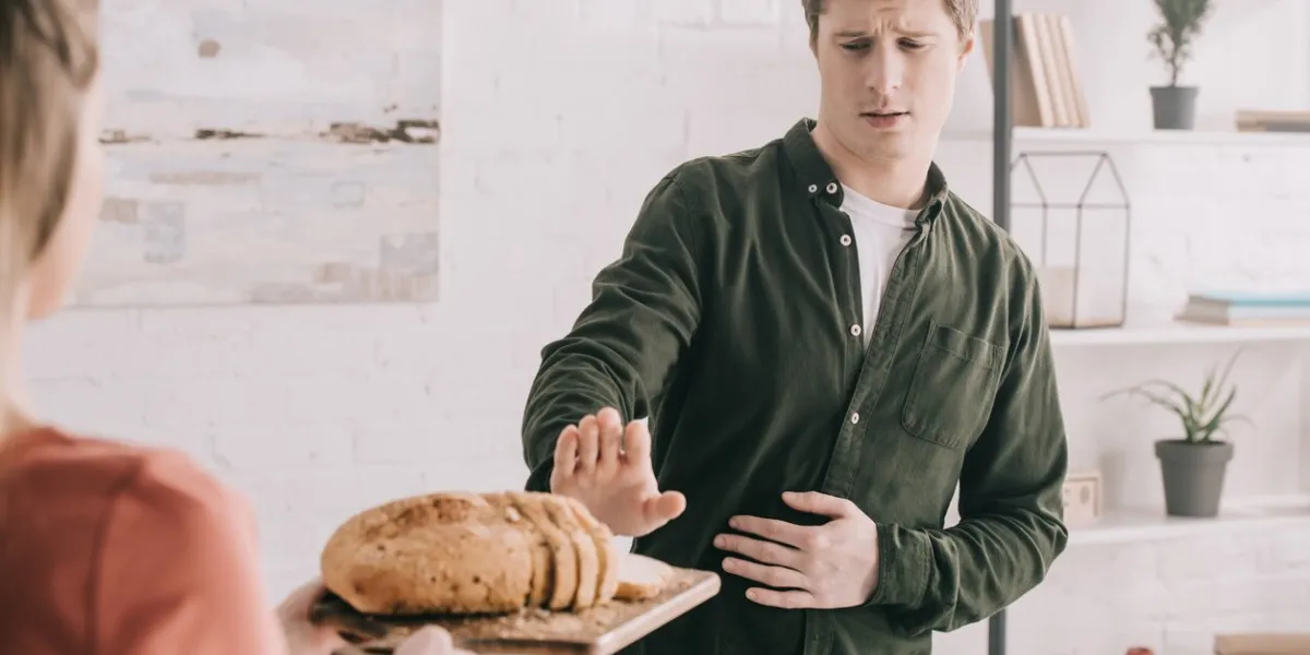 cropped view of woman holding cutting board with sliced bread near handsome man with gluten allergy
