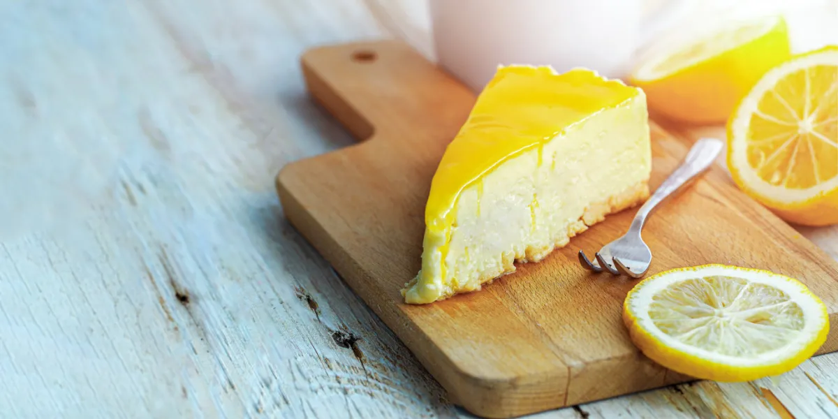 lemon cheesecake is served on a wooden chopping board and slice of lemon beside