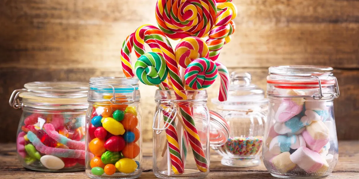 colorful candies, jellies, lollipops, marshmallows and marmalade in a glass jars on wooden table