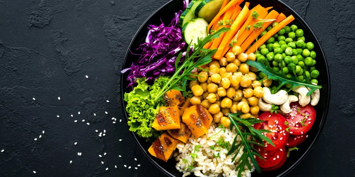 bowl dish with brown rice, cucumber, tomato, green peas, red cabbage, chickpea, fresh lettuce salad and cashew nuts healthy balanced eating