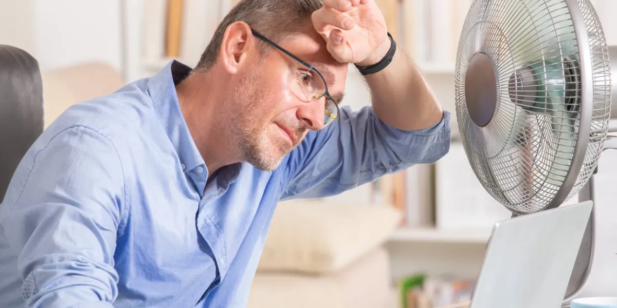 man suffers from heat while working in the office and tries to cool off by the fan