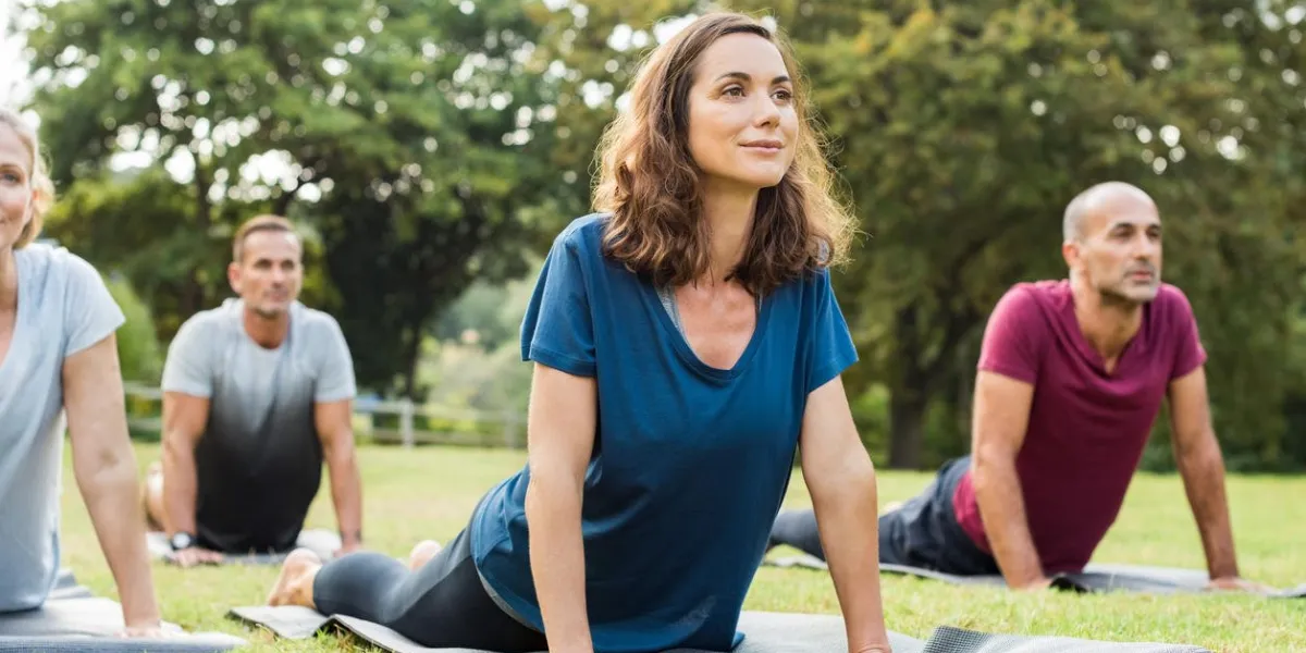 mature healthy people doing yoga at park group of multiethnic people exercising on green grass with yoga mat happy men and smiling women in yoga class doing exercise outdoorr