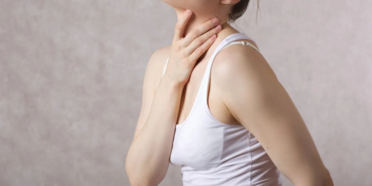 a young woman between 30 and 40 years old shows that she has a pain in the throat free space for a text