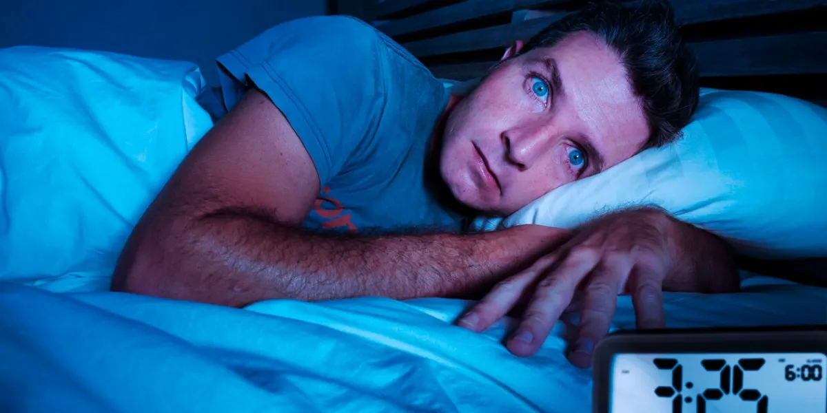 restless worried young attractive man awake at night lying on bed sleepless with eyes wide opened suffering insomnia sleeping disorder depressed and sad in rest privation stress concept