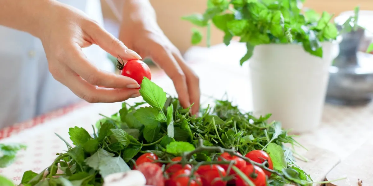 woman is cooking in home kitchen female hands choose cherry tomatoes, vegetables for recipe ingredients for preparing italian or french food are on table on wooden boards lifestyle moment close up