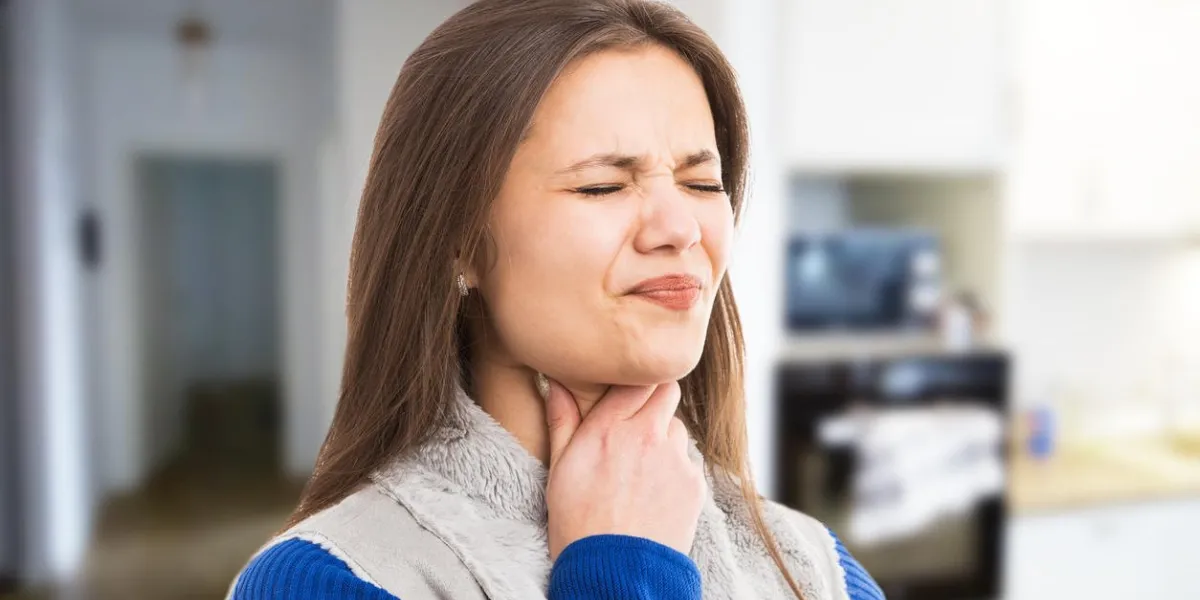 young woman experiencing strong throat ache because of flu cold as swallowing discomfort expression concept on indoor room background