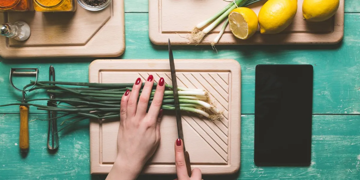 female person cutting fresh spring onion on a blue wooden table view from above