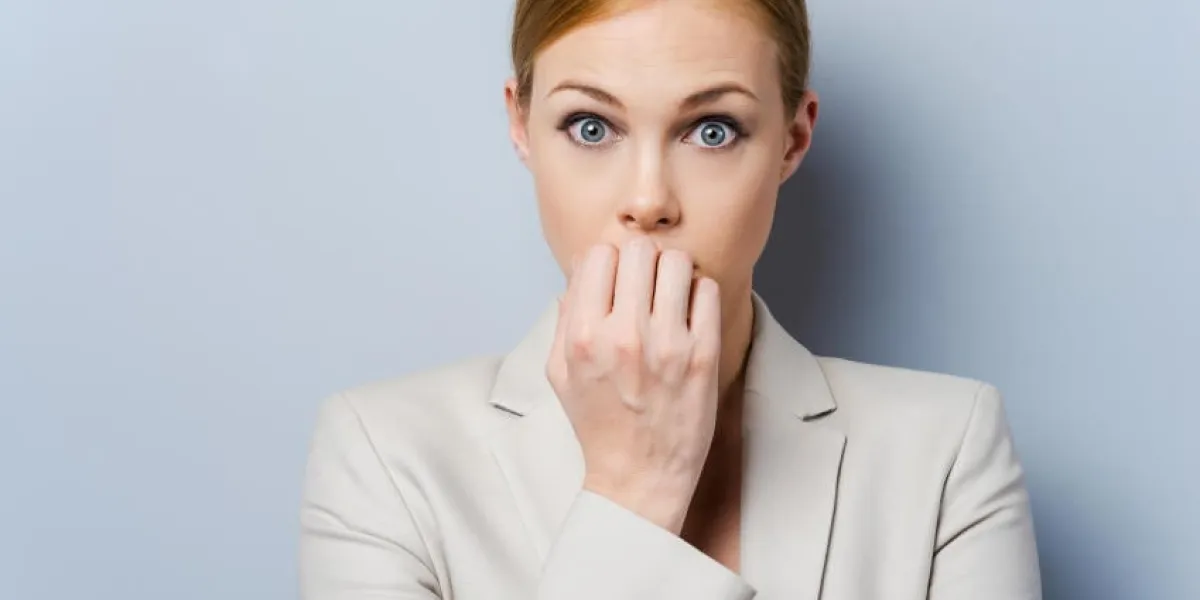 un peu nerveux nerveux jeune femme d'affaires se ronger les ongles en se tenant debout sur fond gris