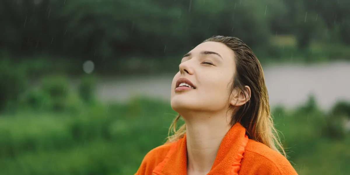 portrait of a young girl in an orange sweater enjoying the rain on a summer day the girl is having fun and dancing under the summer rain
