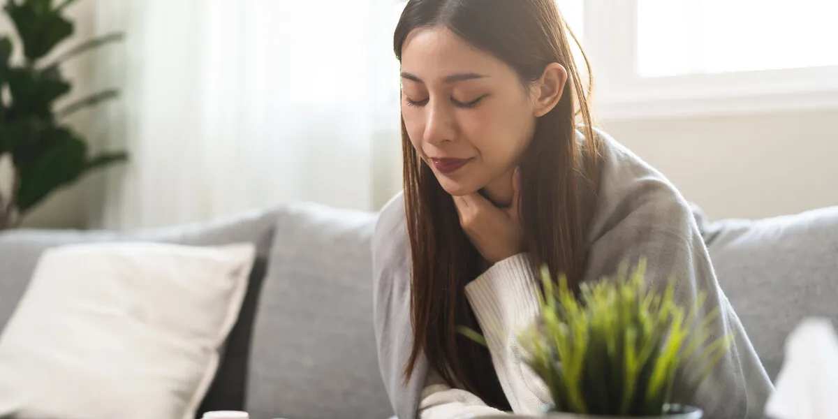 sick, hurt or pain asian young woman, girl with sore throat, cough have a fever, flu and sneezing nose, runny sitting on sofa bed at home health care person on virus seasonal
