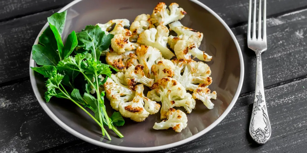 chou-fleur rôti et salade verte fraîche sur une plaque brune sur un fond en bois foncé