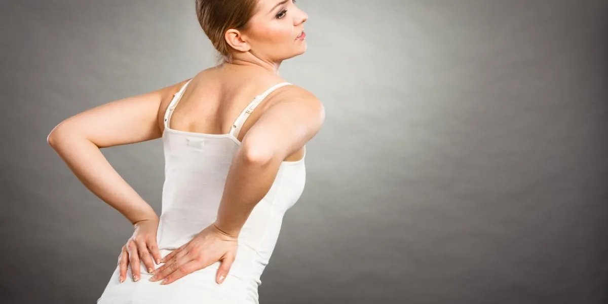 long working hours and health young female with backache woman suffering from back pain on gray