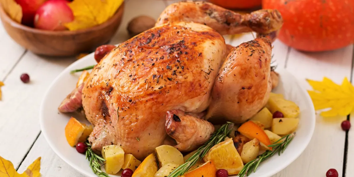 roasted turkey garnished with cranberries on a rustic style table decorated with pumpkins, orange, apples and autumn leaf thanksgiving day