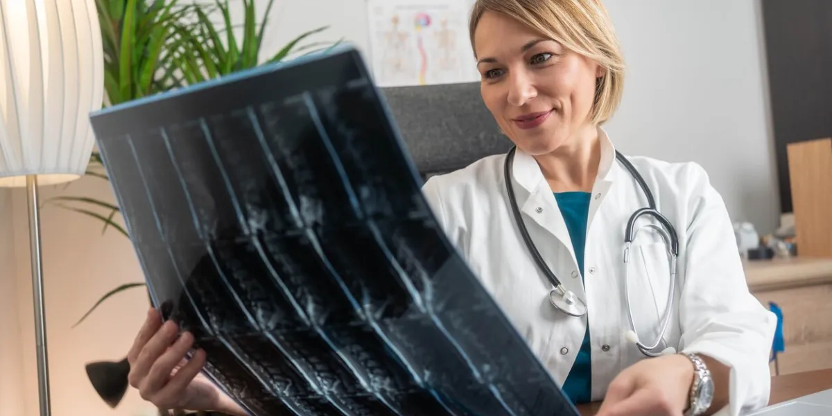 a beautiful middle-aged female doctor carefully examines an mri scan of the spine in her modern medical office, focused on the details of the image for diagnosis