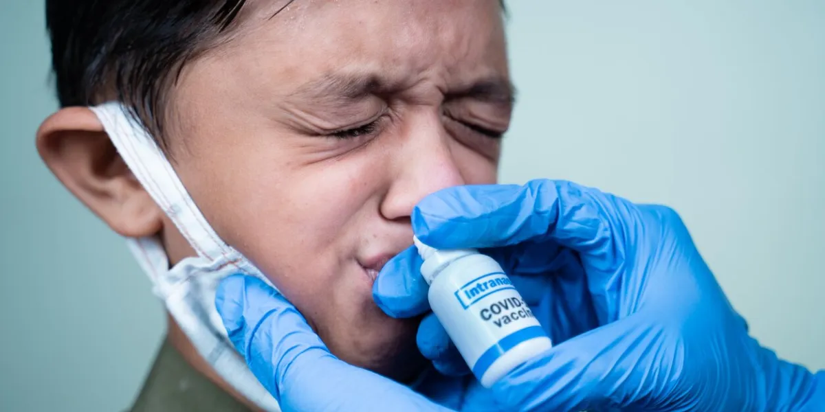 head shot of child with medical face mask getting intranasal coronavirus covid-19 vaccination through nostril from doctor - concept of covid nasal vaccine