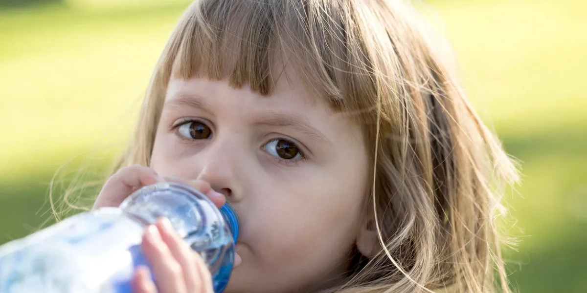 petite fille boit de l'eau et regarde la caméra