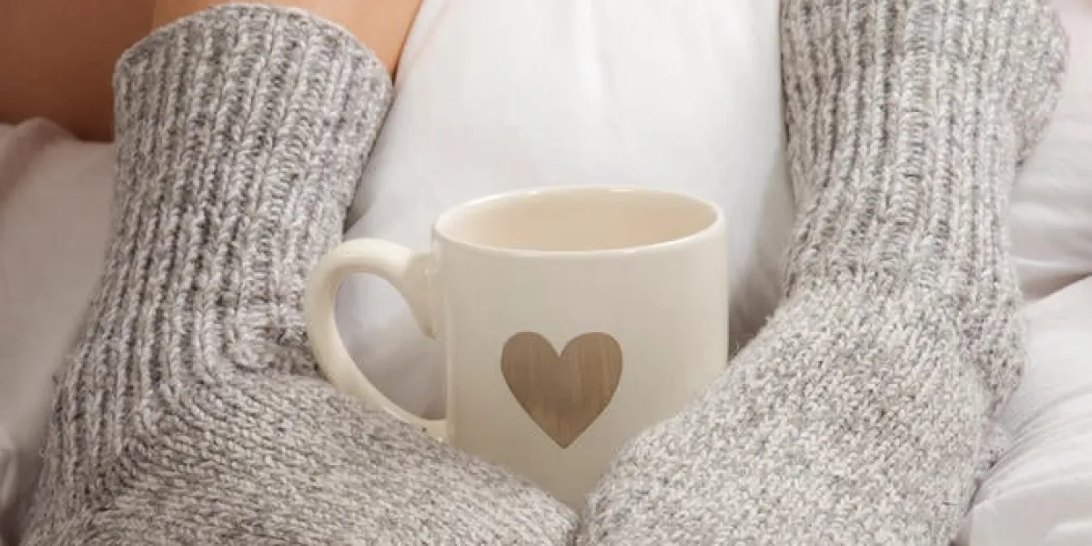 une tasse de café ou de chocolat chaud et des pieds féminins avec des chaussettes sur des draps blancs