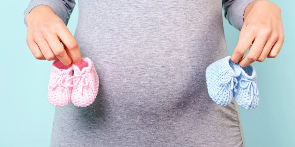 photo d'une femme enceinte de 32 semaines tenant des chaussons de bébé, rose pour une fille et bleu pour un garçon