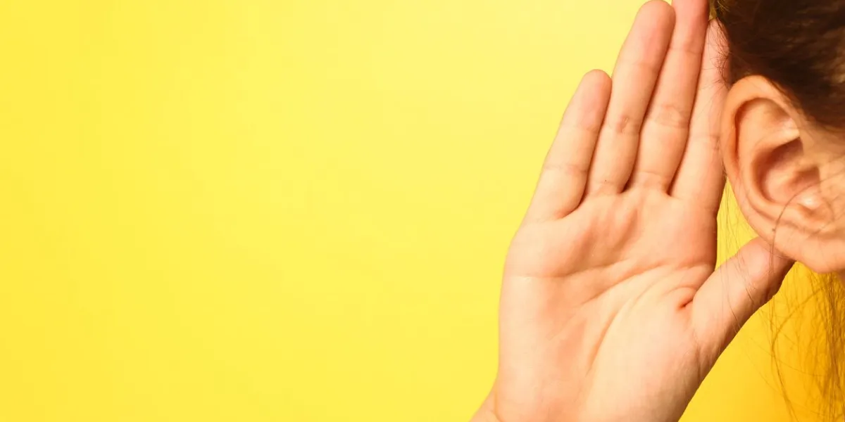 girl holds her hand near ear and listens carefully isolated on wall background
