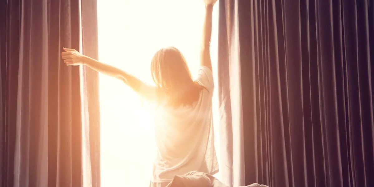 femme debout près de la fenêtre tout en étirant près du lit après le réveil avec le lever du soleil au matin, vue de dos