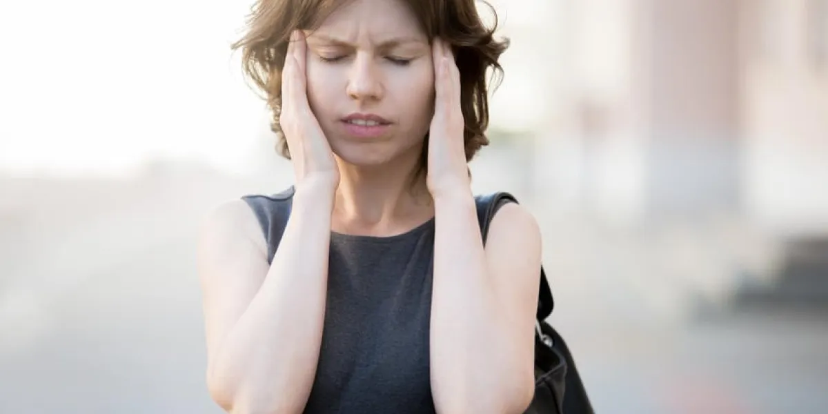 portrait de jeune femme marchant dans la rue en été, fronçant les sourcils, tenant sa tête dans les mains, ayant mal à la tête, tension artérielle basse ou élevée, stress