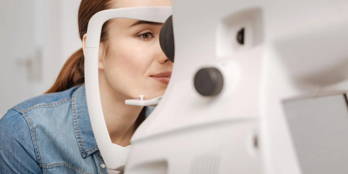 se soucier de la santé attrayant agréable agréable femme assise devant le dispositif d'examen de l'oeil et regarder dedans tout en vérifiant sa vue